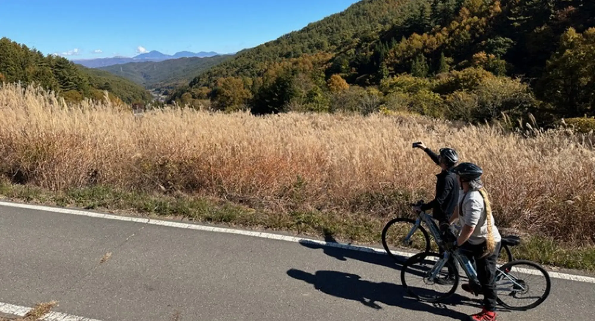 A couple wearing helmets is riding bicycles and pointing at a mountain while talking.