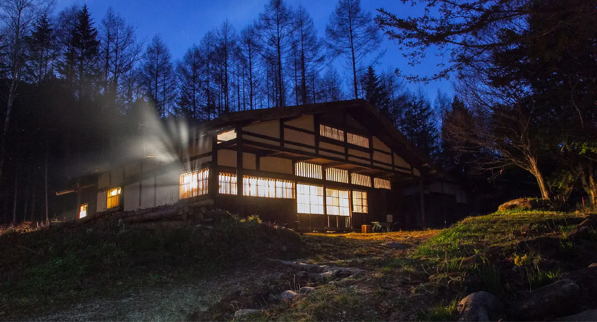 A traditional Japanese house with lit lanterns in a forest after sunset