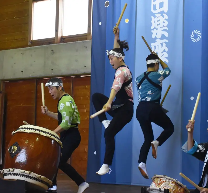 Men and women wearing headbands, playing taiko drums while jumping