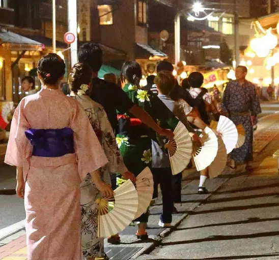 Women and men wearing yukata and holding fans, dancing in a line at a festival