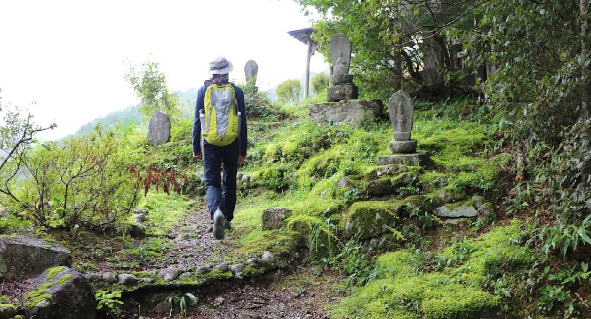 A woman wearing a hat and carrying a backpack is exploring an open mountain.