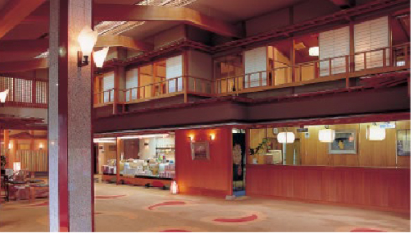 The interior of a ryokan lobby, showcasing traditional wooden architecture with warm lighting, tatami flooring, and a spacious open design