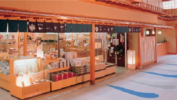 A souvenir shop inside the ryokan, selling traditional Japanese items and local specialties. The shop has a warm wooden aesthetic with noren curtains.