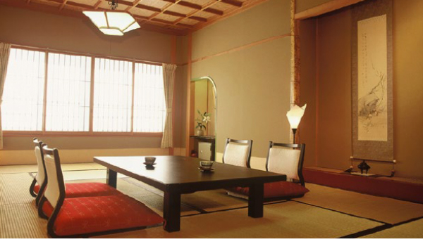 A Japanese-style tatami room featuring a low wooden table, red cushions, and a hanging scroll on the wall, providing an authentic ryokan experience.