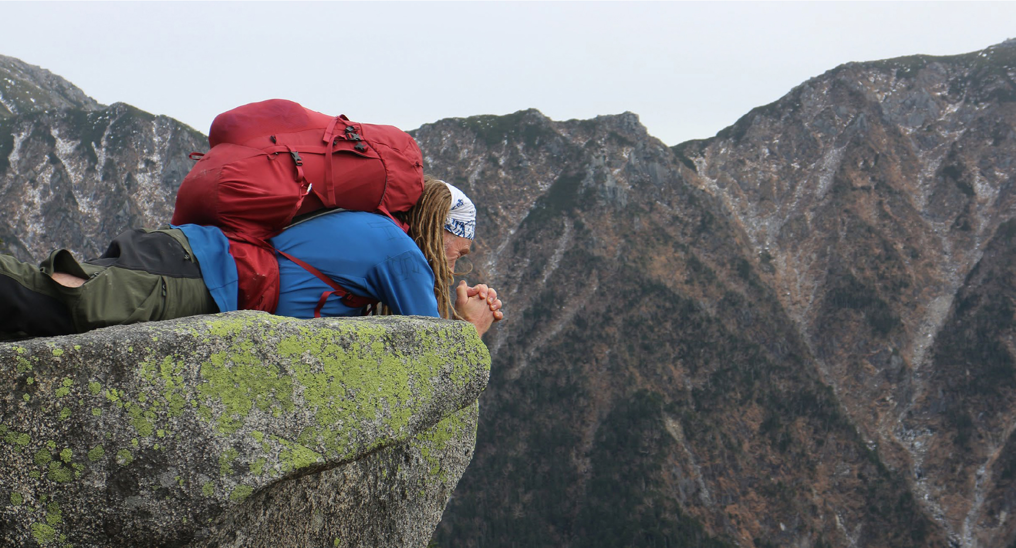 A backpacker lying on a moss-covered rock at the edge of a cliff, enjoying the breathtaking mountain view.