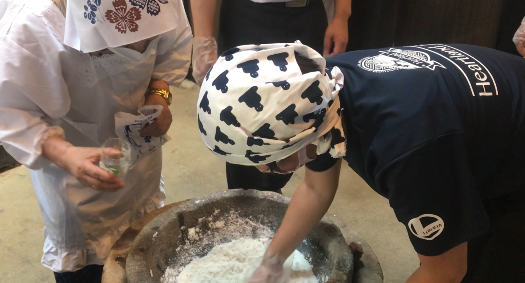 Participants in traditional attire engaging in a hands-on mochi-making experience, kneading glutinous rice in a stone mortar with a wooden pestle.