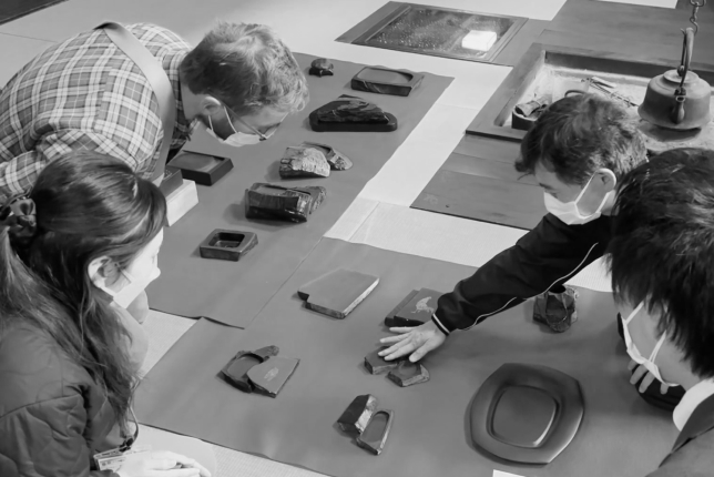 A group of people sitting on the floor examining various types of traditional Japanese inkstones. An instructor points at the stones while explaining their details.