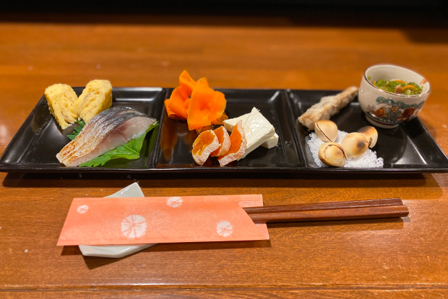 A beautifully arranged plate featuring Japanese appetizers, including grilled fish, tamagoyaki, and pickled vegetables.