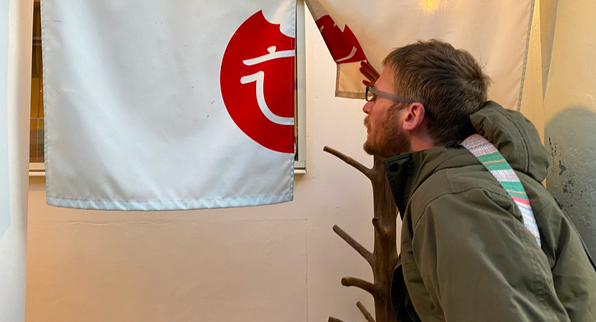 A man peeks into a shop or restaurant through a noren (traditional Japanese fabric divider) with a red circular logo, curiously observing the interior.