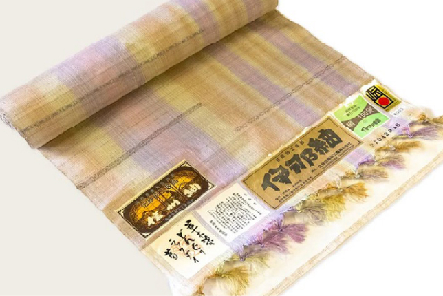 A beautifully handwoven silk fabric roll with natural pastel hues. The label indicates its authenticity as a traditional Japanese textile.