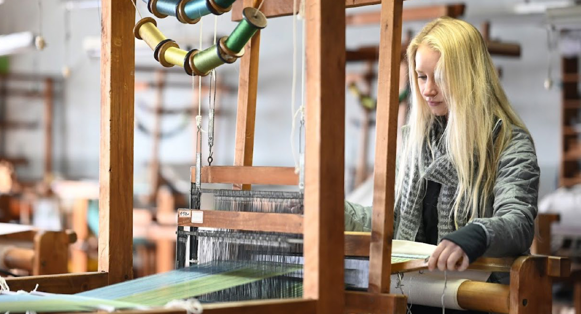 A visitor engaged in a hands-on weaving experience, working on a wooden loom with vibrant silk threads. The workshop provides an immersive look into traditional Japanese textile making.