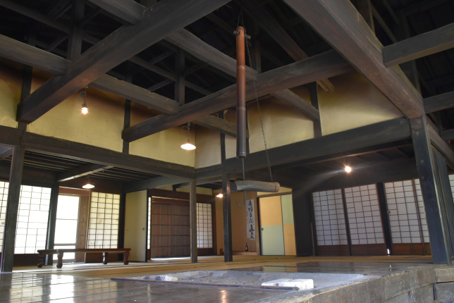 The interior of a traditional Japanese house featuring a sunken hearth (irori), wooden beams, and tatami flooring.