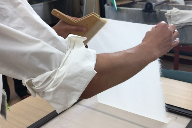 A craftsman carefully presses and smooths a freshly made sheet of washi paper onto a drying surface.