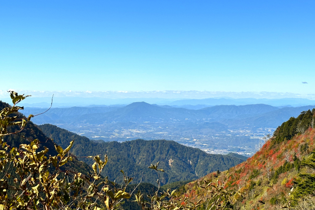 A scenic view from a mountain peak, overlooking vast landscapes with distant mountains under a clear blue sky.