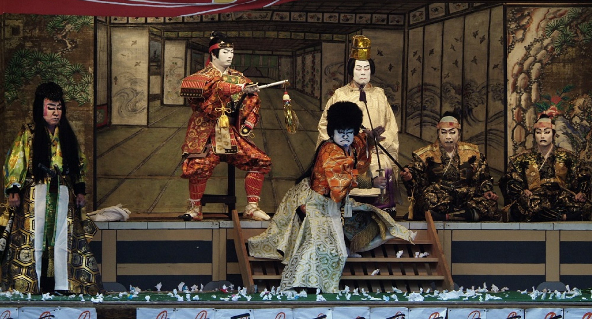 A traditional Japanese kabuki play performed on a stage with elaborate costumes and dramatic expressions, depicting a historical or mythological story.