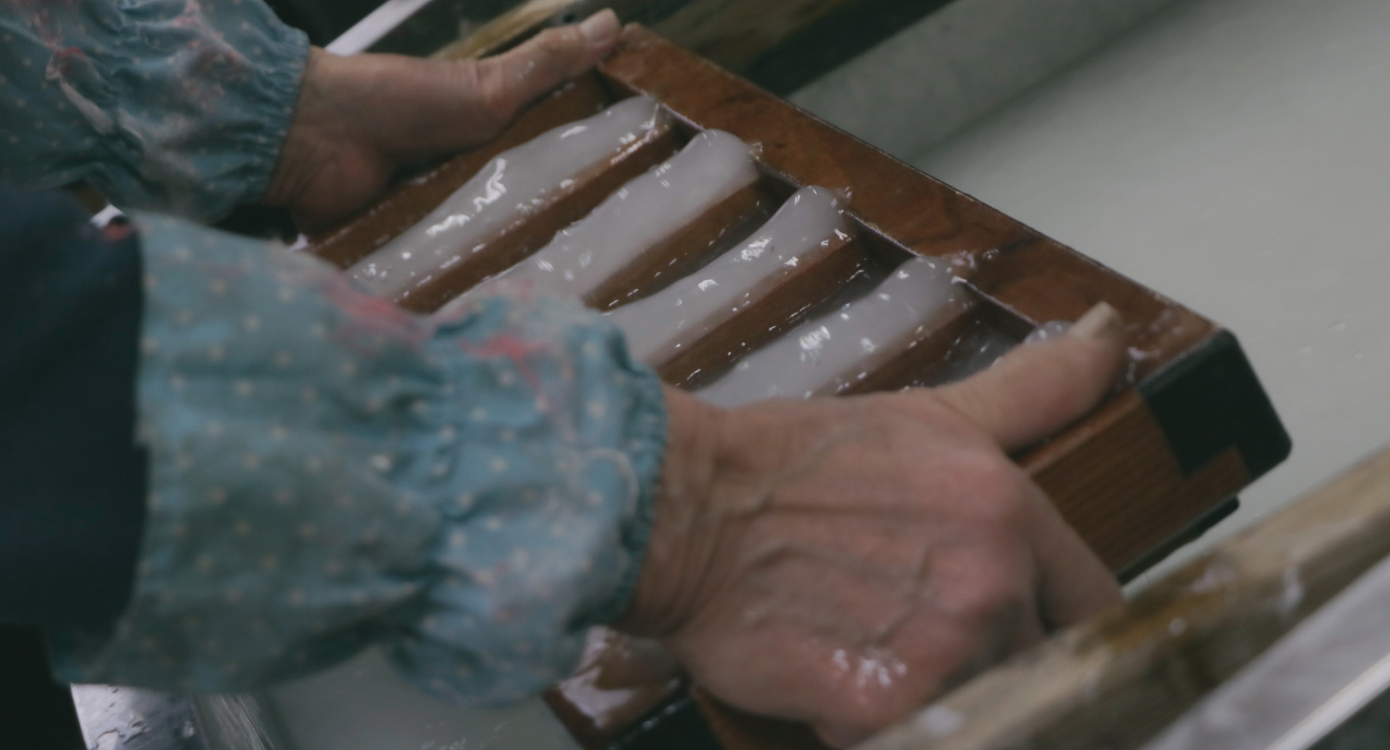 A craftsman shaping handmade washi paper using a wooden mold, with water and paper pulp forming delicate sheets.