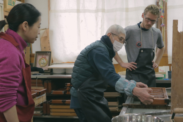 A craftsman demonstrating the traditional process of making Japanese washi paper, with visitors attentively observing the technique.