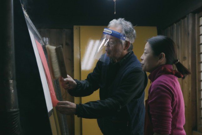 A craftsman using a brush to smooth and dry a freshly made washi paper sheet, ensuring its quality and texture.